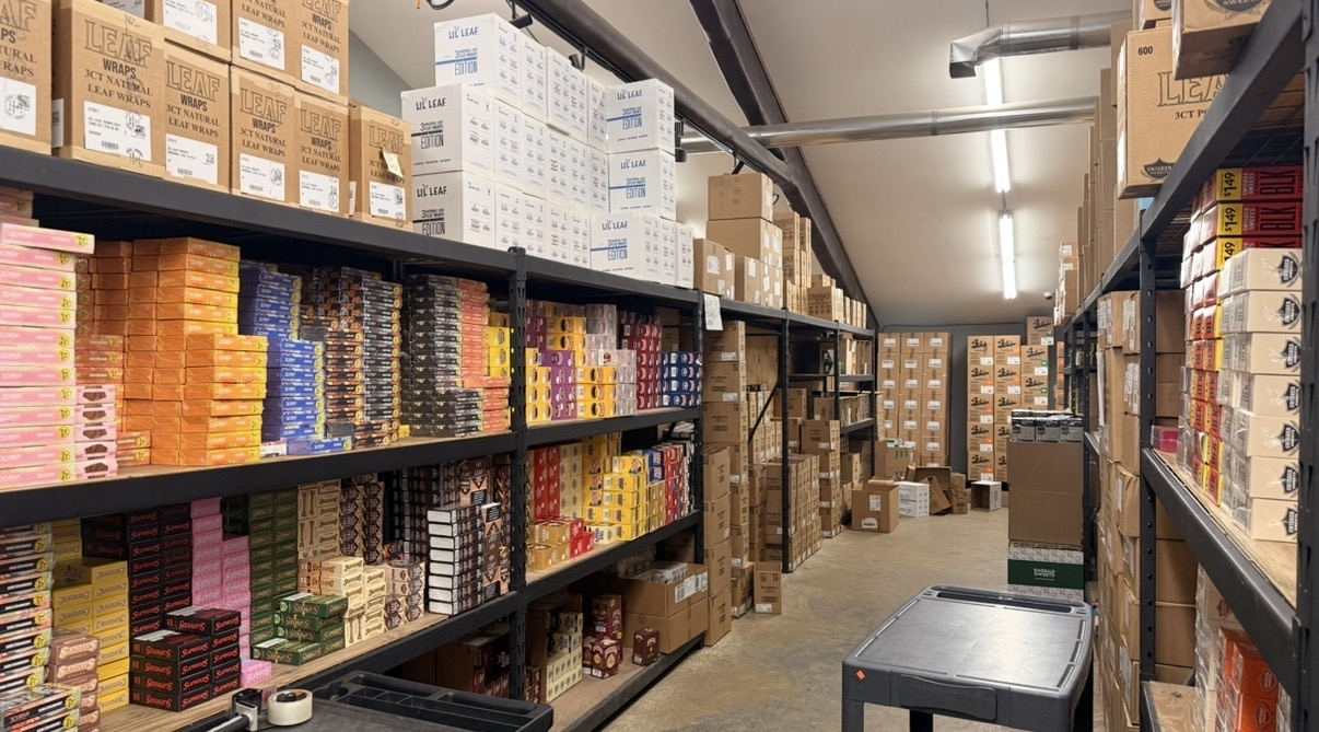 A stocked Lambert's warehouse aisle with colorful tobacco and wholesale sundries organized on shelving